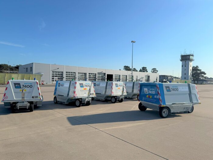 cinco unidades de potencia en tierra itw gse 7400 accionadas por batería en la plataforma con un hangar, una torre de control y un cielo azul al fondo.